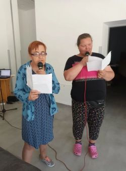 dwie śpiewające stojące osoby trzymające mikrofon oraz kartki